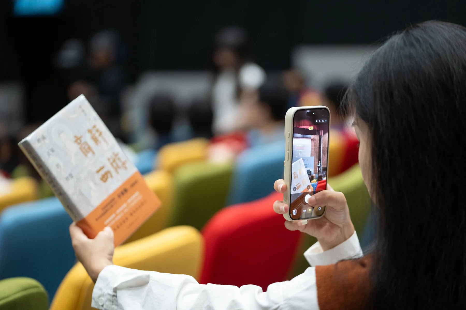 An attendee photographing a dialogue booklet in the auditorium